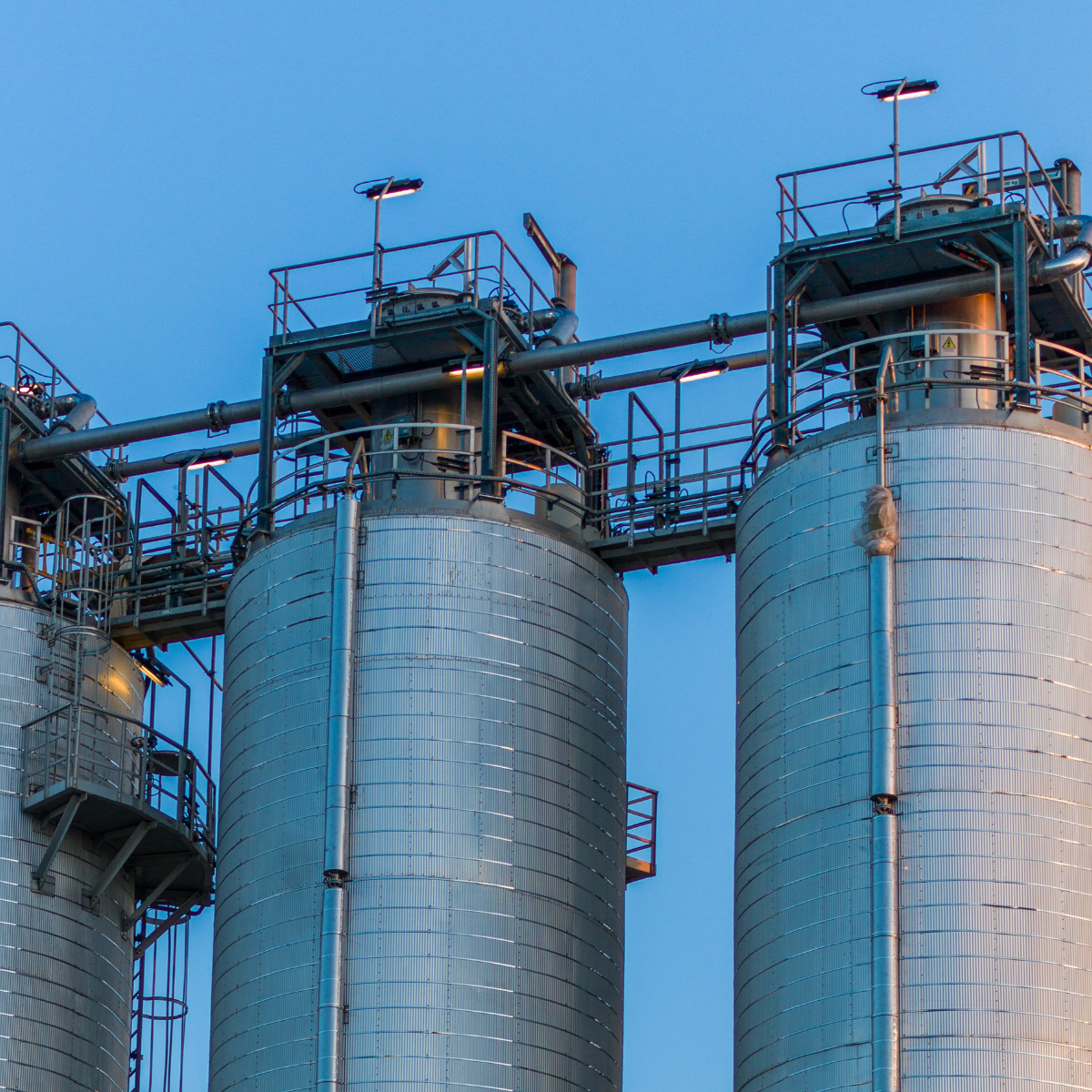 Industrial storage silos for chemical and petrochemical processing, featuring metallic exteriors and connected piping against a clear blue sky.