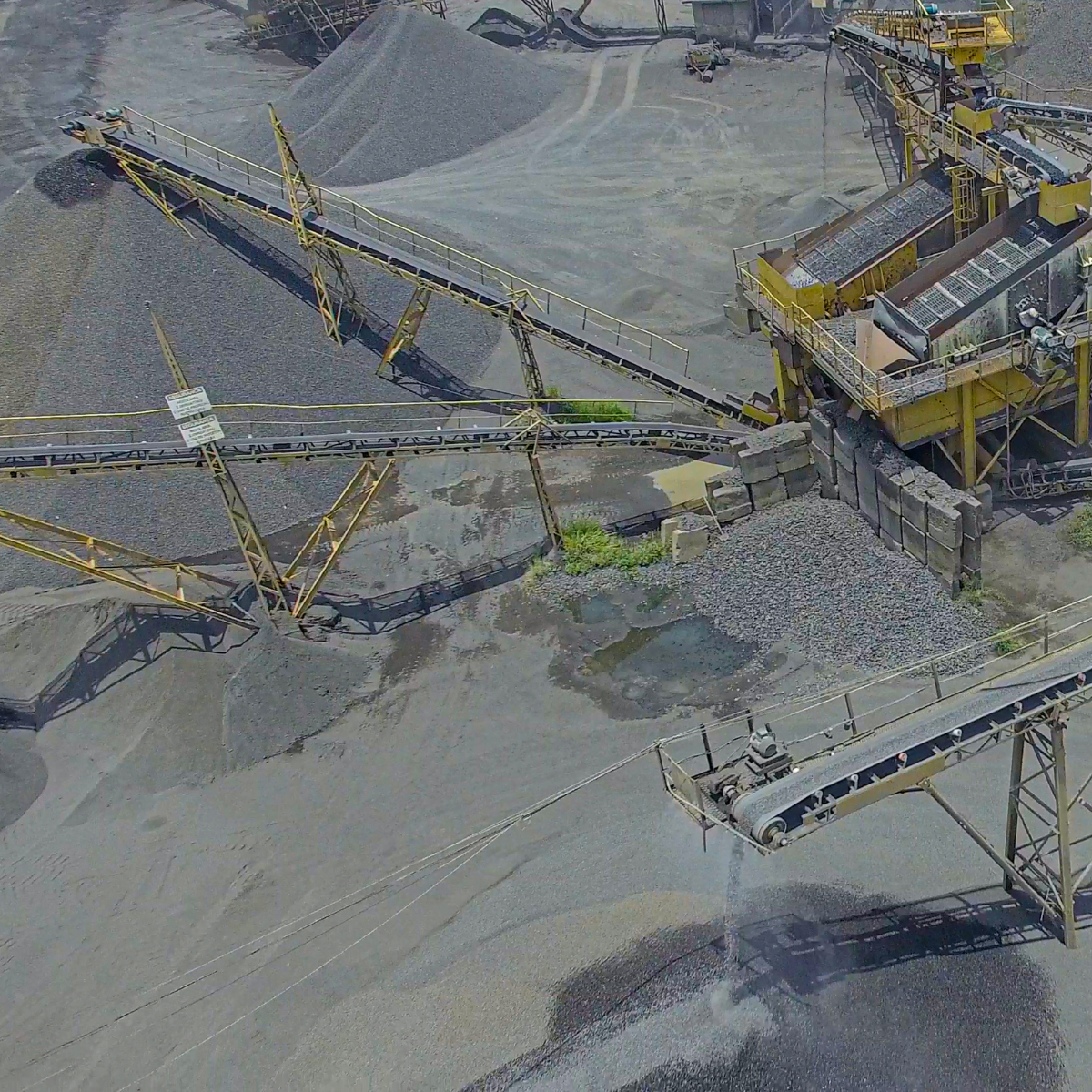 Aerial view of a gravel processing facility featuring multiple conveyor belts transporting materials, with large piles of gravel in the background, illustrating industrial operations in material handling and processing.