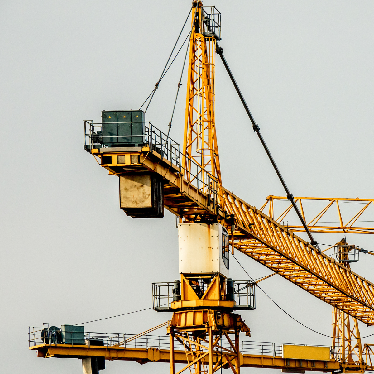 Close-up view of a yellow construction crane, showcasing its operator cabin, boom, and structural components against a gray sky, illustrating the machinery used in building and construction projects.