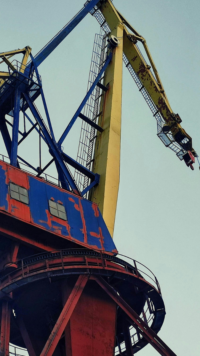 Industrial crane with a blue and yellow structure, showcasing its cab and lifting arm against a clear sky. Ideal for construction and heavy lifting applications.