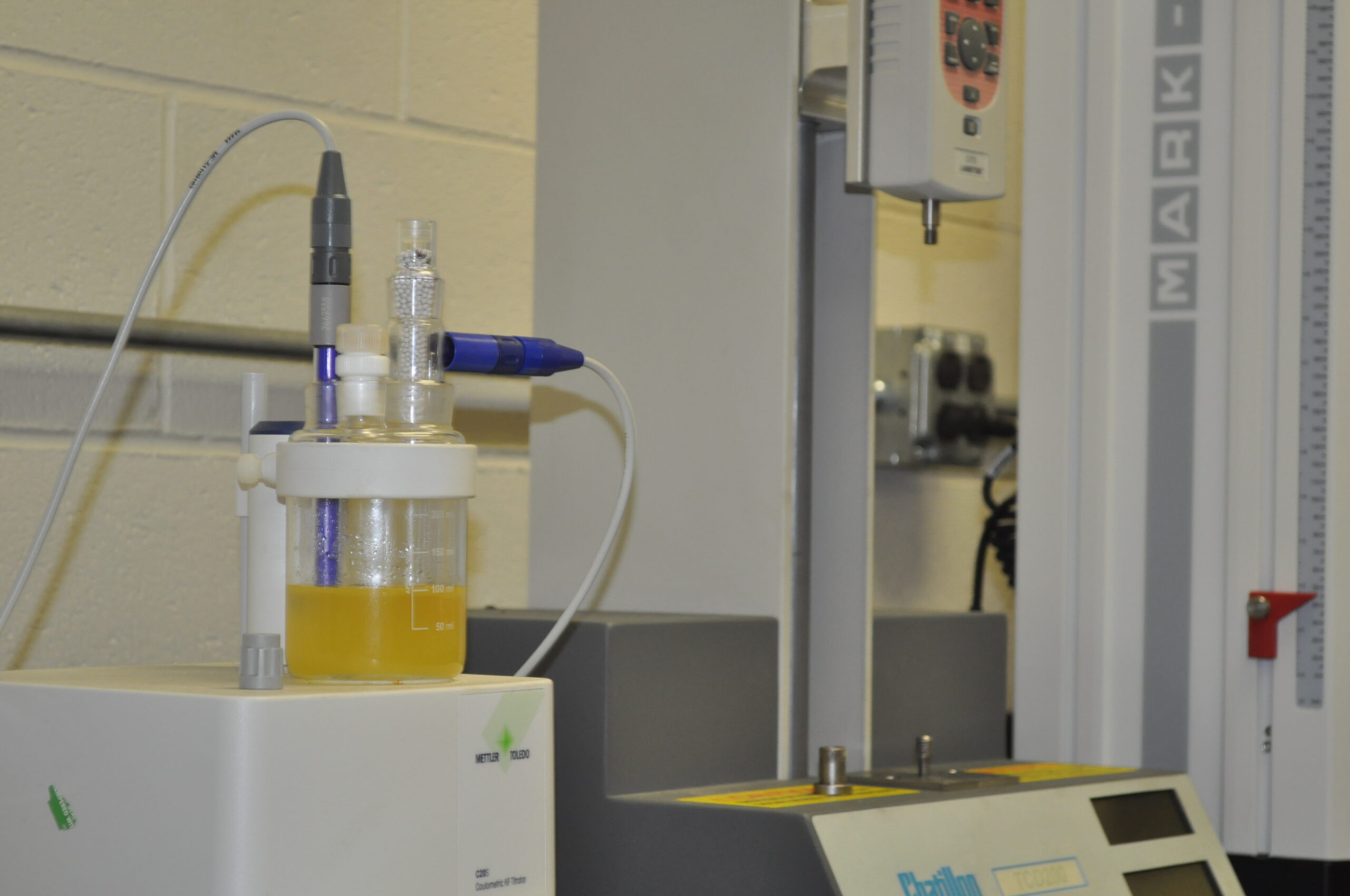 Laboratory setup for filter cartridge testing, featuring a glass container with yellow liquid, connected to measurement instruments for precise analysis.