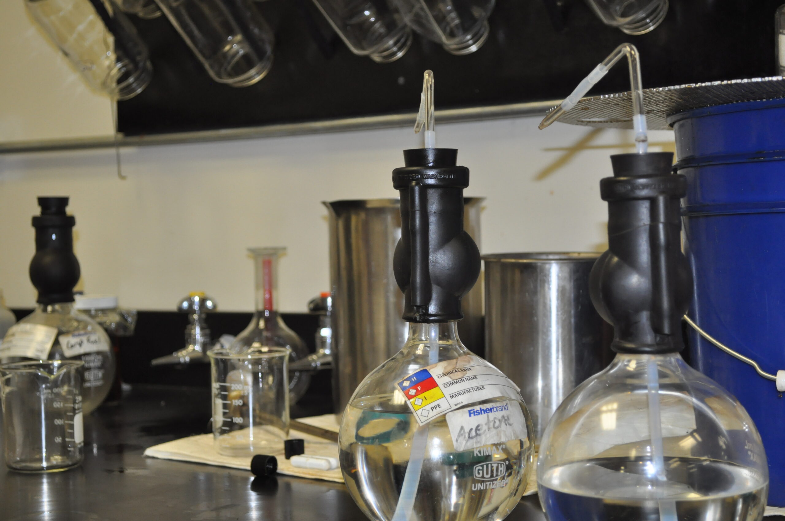 Laboratory setup for fluid sample analysis featuring various glassware, including flasks and beakers, with acetone labeled, and a black vacuum pump, showcasing a clean and organized research environment.