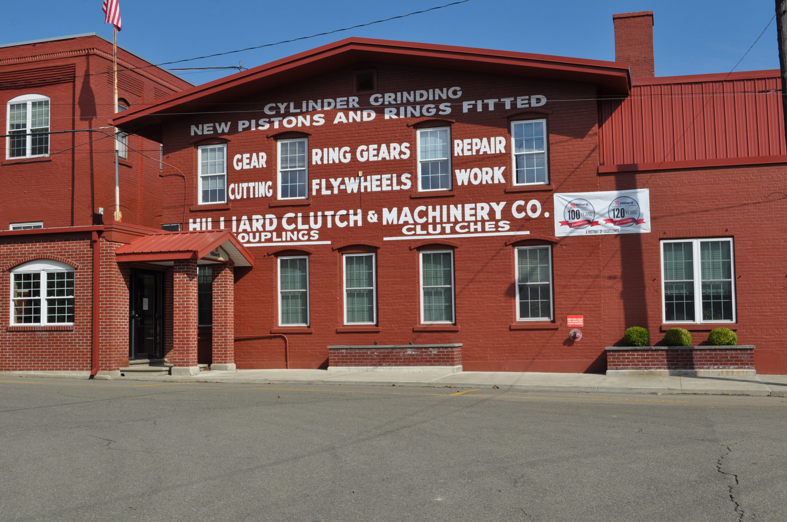 Exterior view of Hilliard Clutch & Machinery Co. building featuring signage about services like cylinder grinding, gear cutting, and clutch repairs, with a banner celebrating over 100 years in business.