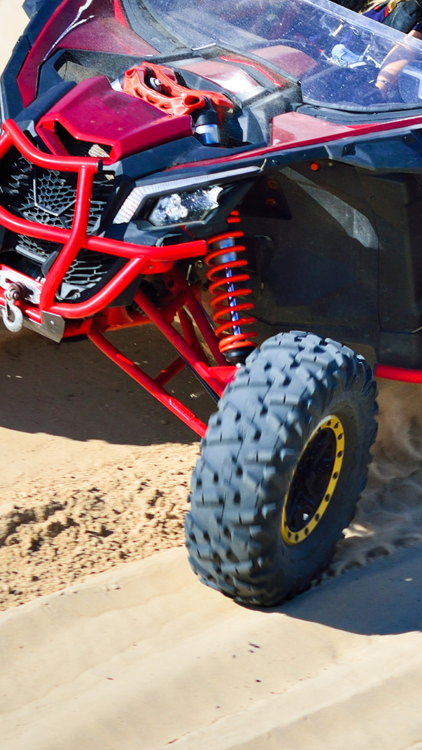 Off-road vehicle navigating sandy terrain, showcasing a front drive system with highlighted differential components and rugged tires designed for enhanced traction and performance.