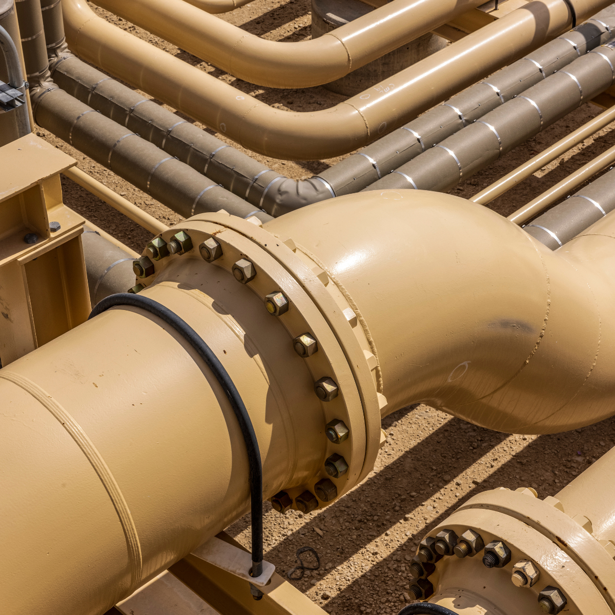 Close-up view of interconnected gas compression pipes and fittings, showcasing a network of beige pipelines with visible bolts and seals, essential for efficient gas transport and compression systems.