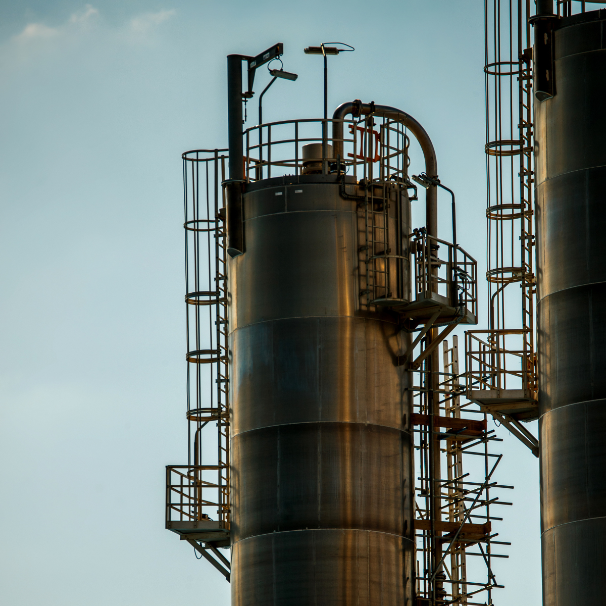 Close-up of industrial gas compression towers with metallic structures and safety railings against a clear sky, illustrating the technology used in gas processing facilities.