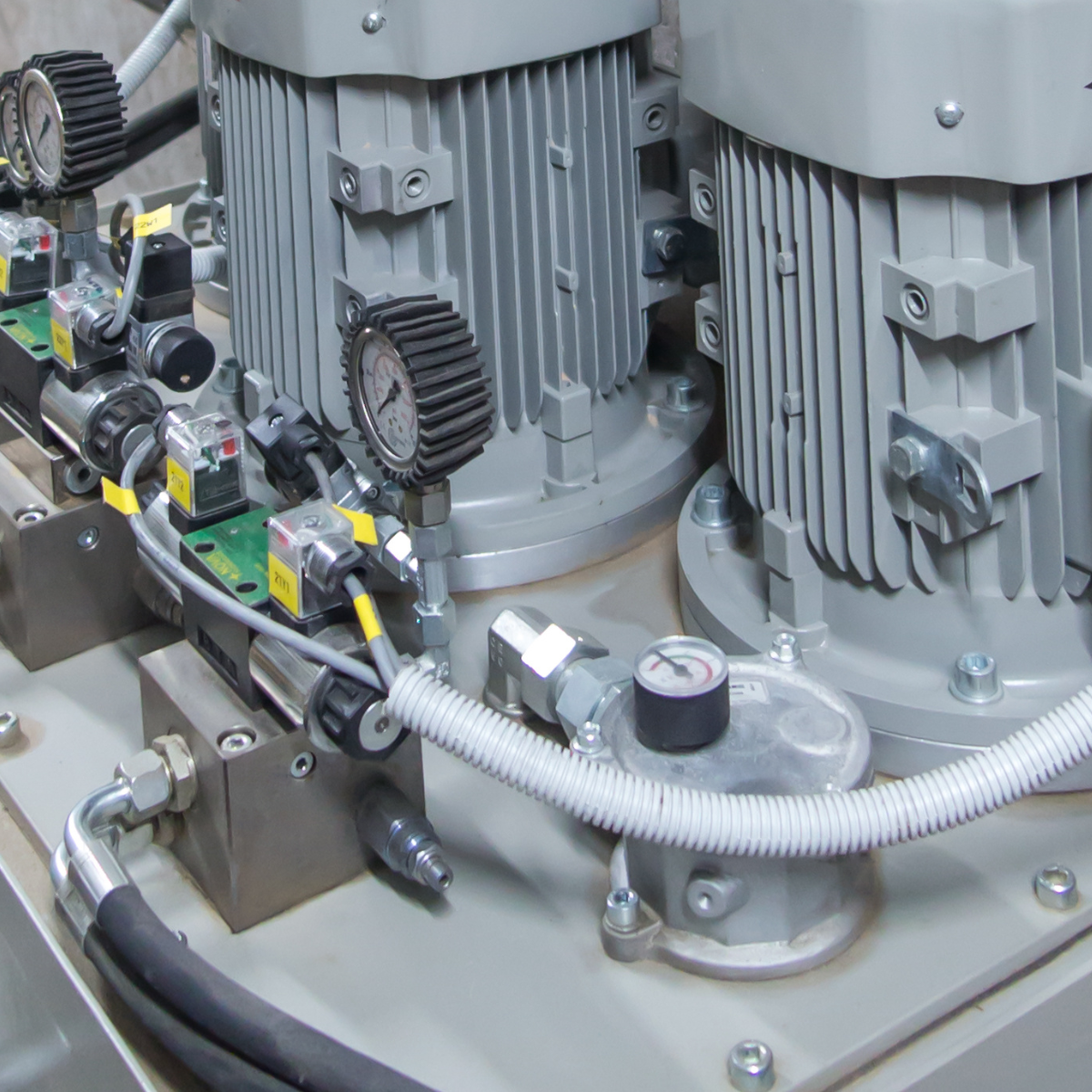Close-up of hydraulic system components featuring two electric motors, pressure gauges, and various valves, illustrating the setup for HP hydraulic fluid applications in industrial machinery.