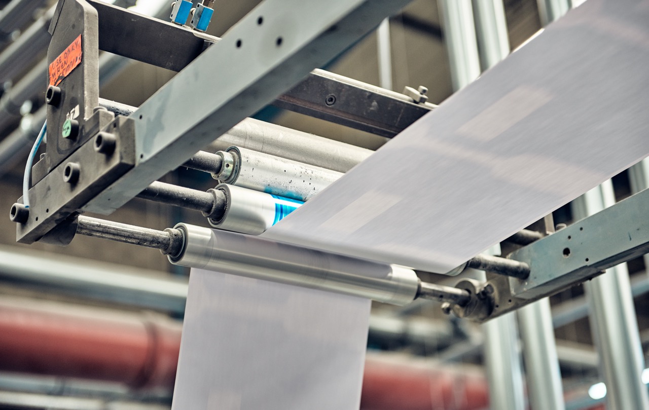 Industrial printing process showcasing large rolls of paper moving through a printing machine, highlighting the machinery and equipment used in modern printing technology.
