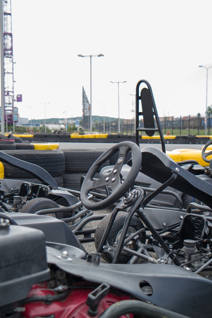 Close-up view of go-karts lined up at a karting track, showcasing steering wheels and chassis against a backdrop of tire barriers and a cloudy sky. Ideal for karting enthusiasts and racing events.