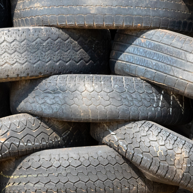 Stacked used tires in a landfill, showcasing various tread patterns and conditions, highlighting the issue of tire waste and environmental impact.