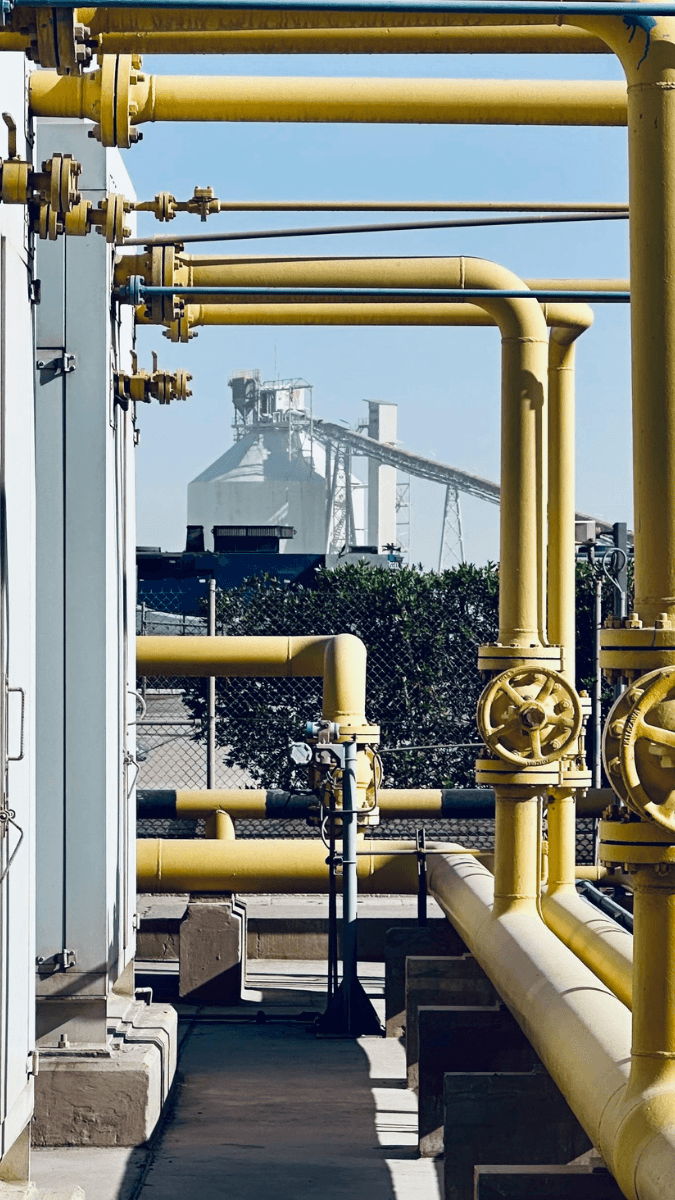 Industrial yellow piping system with valves leading to a processing facility, illustrating liquid coalescing cartridges used in filtration and separation processes.