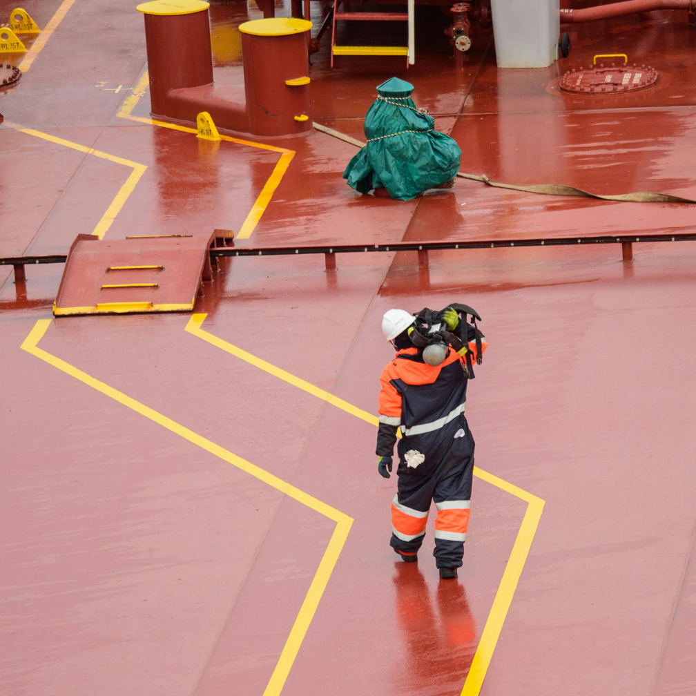 Worker in safety gear walking on a wet ship deck with yellow safety markings, highlighting marine operations and safety protocols in the shipping industry.