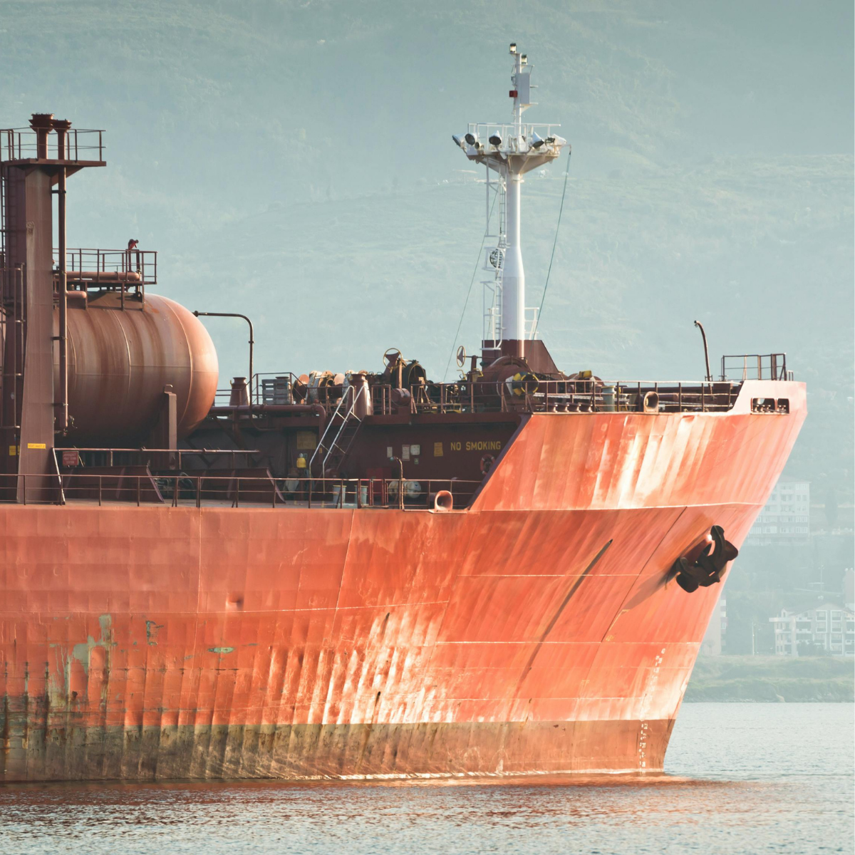 Large cargo ship anchored in calm waters, showcasing its rust-colored hull and industrial features, with a focus on maritime operations and shipping logistics.