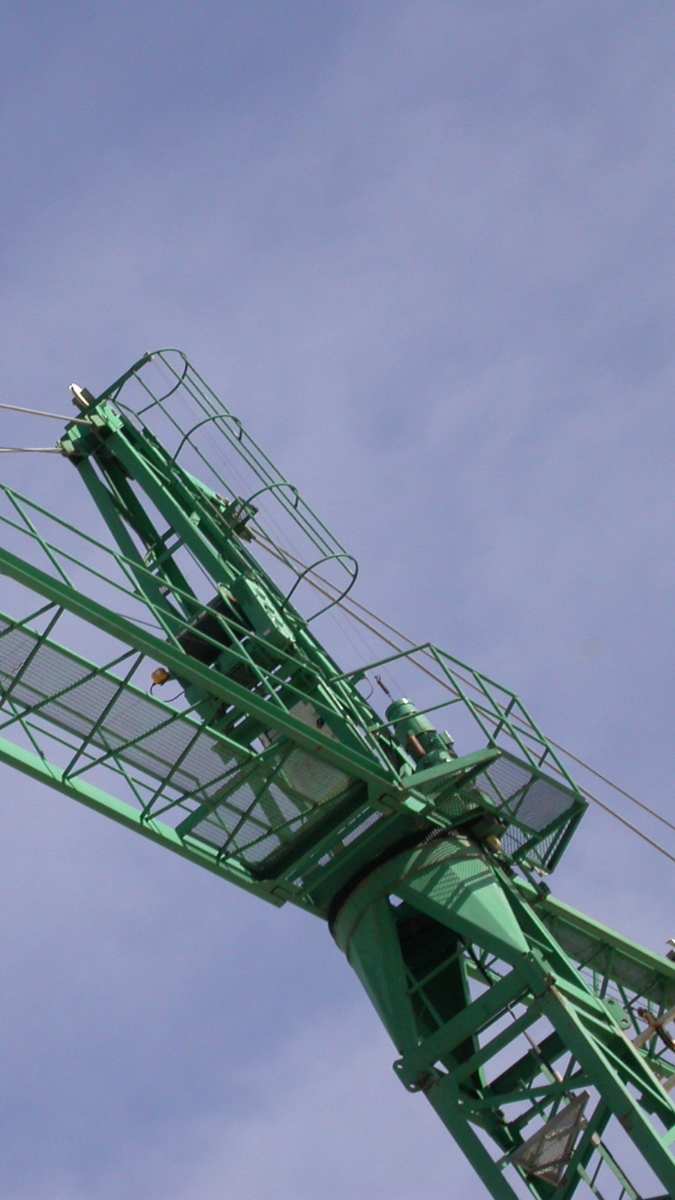 Green construction crane against a blue sky, showcasing its lifting capabilities for material handling in construction projects.