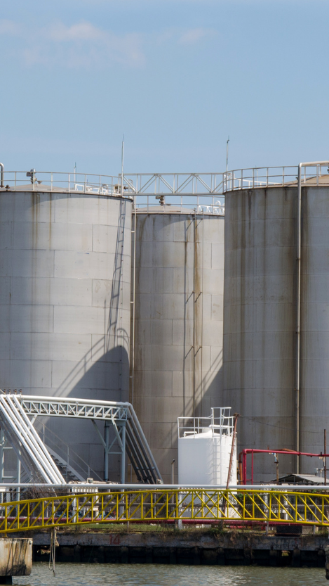 Industrial gas storage tanks near water, showcasing large cylindrical structures with a staircase and piping, relevant to midstream gas operations.