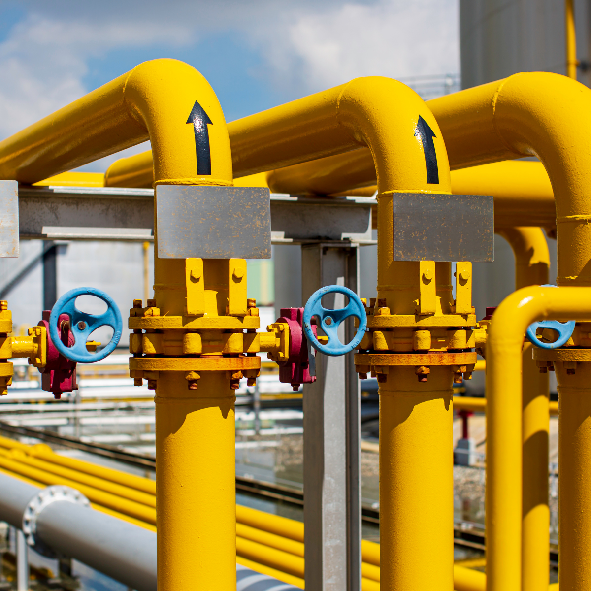 Yellow gas pipelines with valves and directional arrows, showcasing midstream gas infrastructure in an industrial setting.