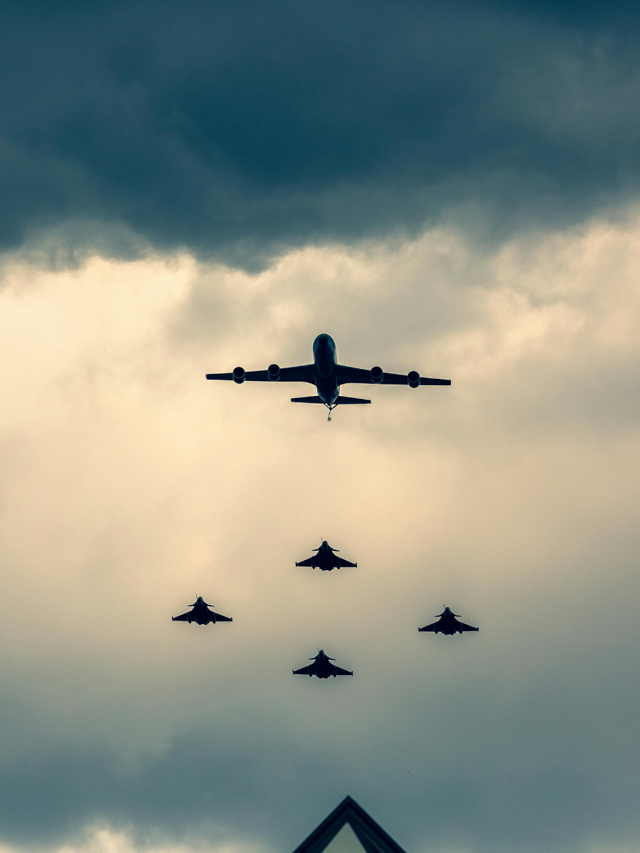 Military aircraft in formation, featuring a large transport plane leading four fighter jets against a dramatic cloudy sky, symbolizing aerial defense and military readiness.