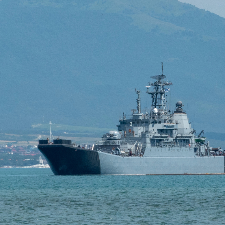 Military naval ship navigating through calm waters with mountains in the background, illustrating modern defense capabilities.