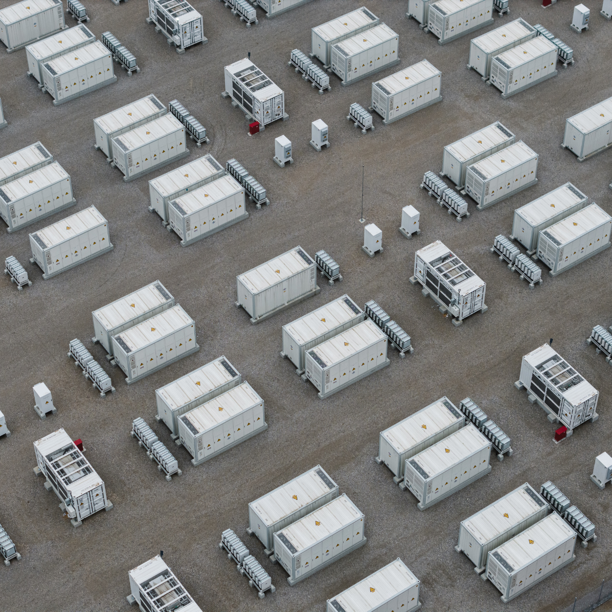 Aerial view of multiple mobile power stations arranged in a grid pattern, featuring white containers with solar panels and energy storage systems on a gravel surface.