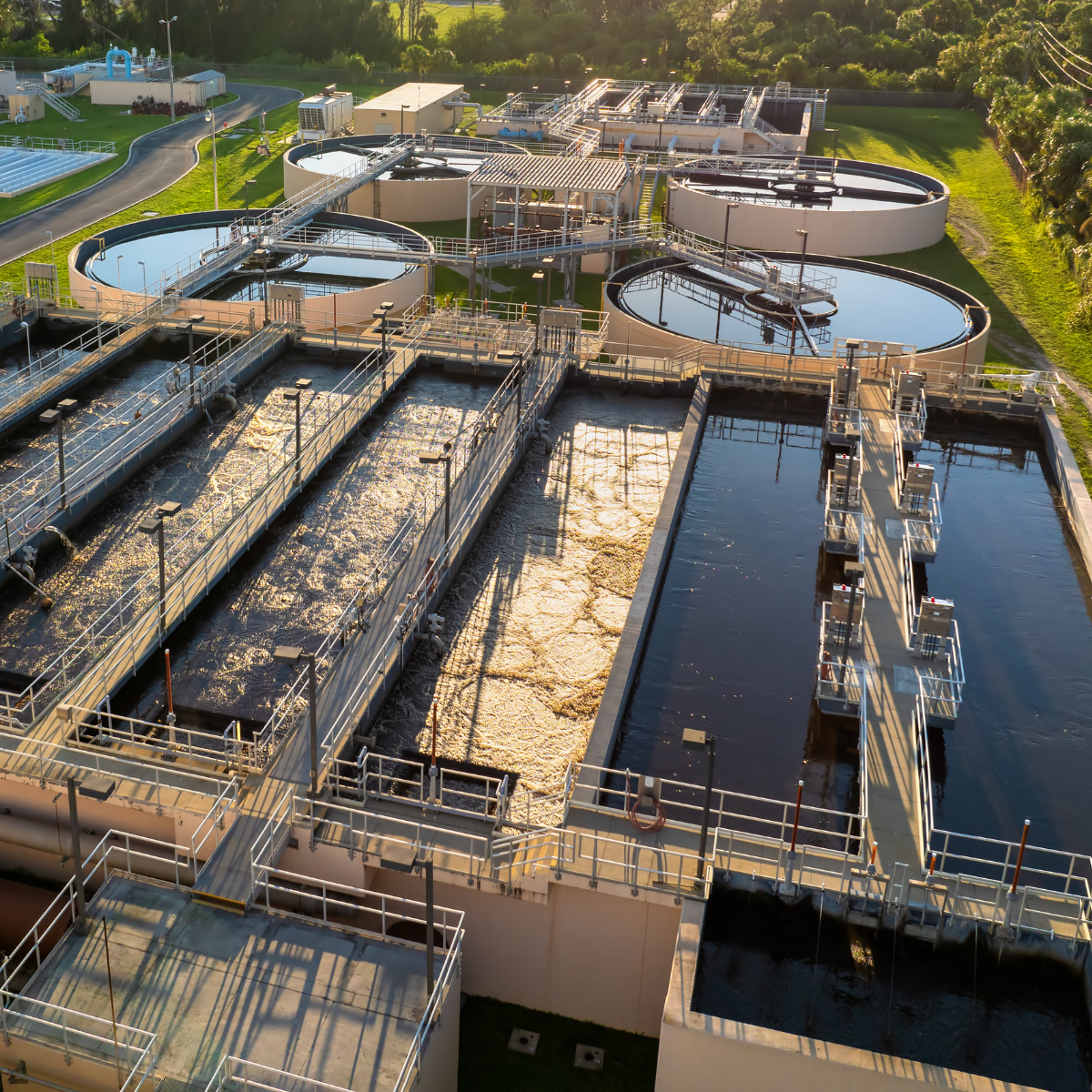 Aerial view of a municipal wastewater treatment facility showcasing multiple circular and rectangular tanks for sewage processing, with clear water in some tanks and aeration equipment visible, highlighting the infrastructure used for municipal utilities management.