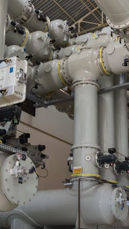 Technician inspecting industrial filter cartridge system with large pipes and valves in a manufacturing facility, emphasizing the importance of filter maintenance and performance.