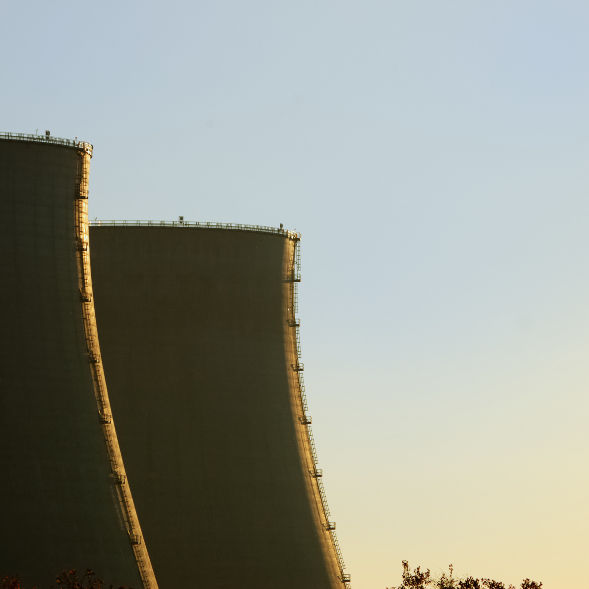 Cooling towers of a nuclear power plant silhouetted against a clear blue sky during sunset, illustrating the infrastructure essential for nuclear energy production.