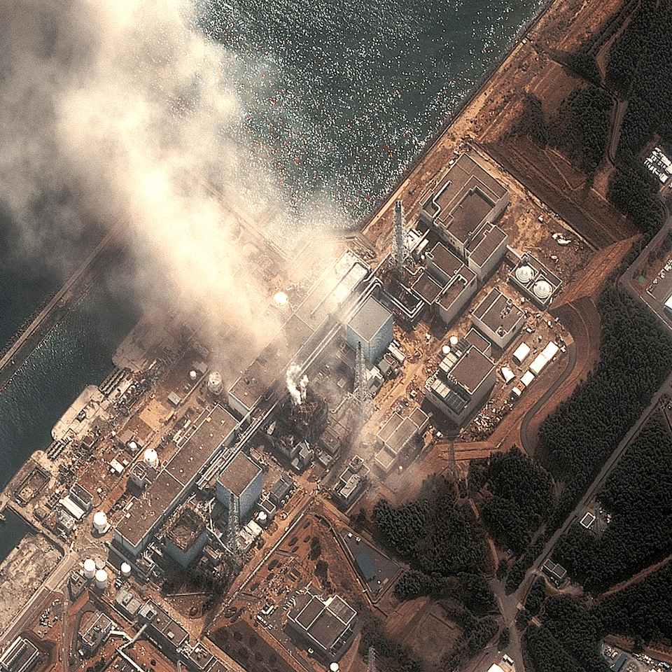 Aerial view of a nuclear power plant emitting steam, surrounded by water and greenery, highlighting the industrial structures and cooling towers.