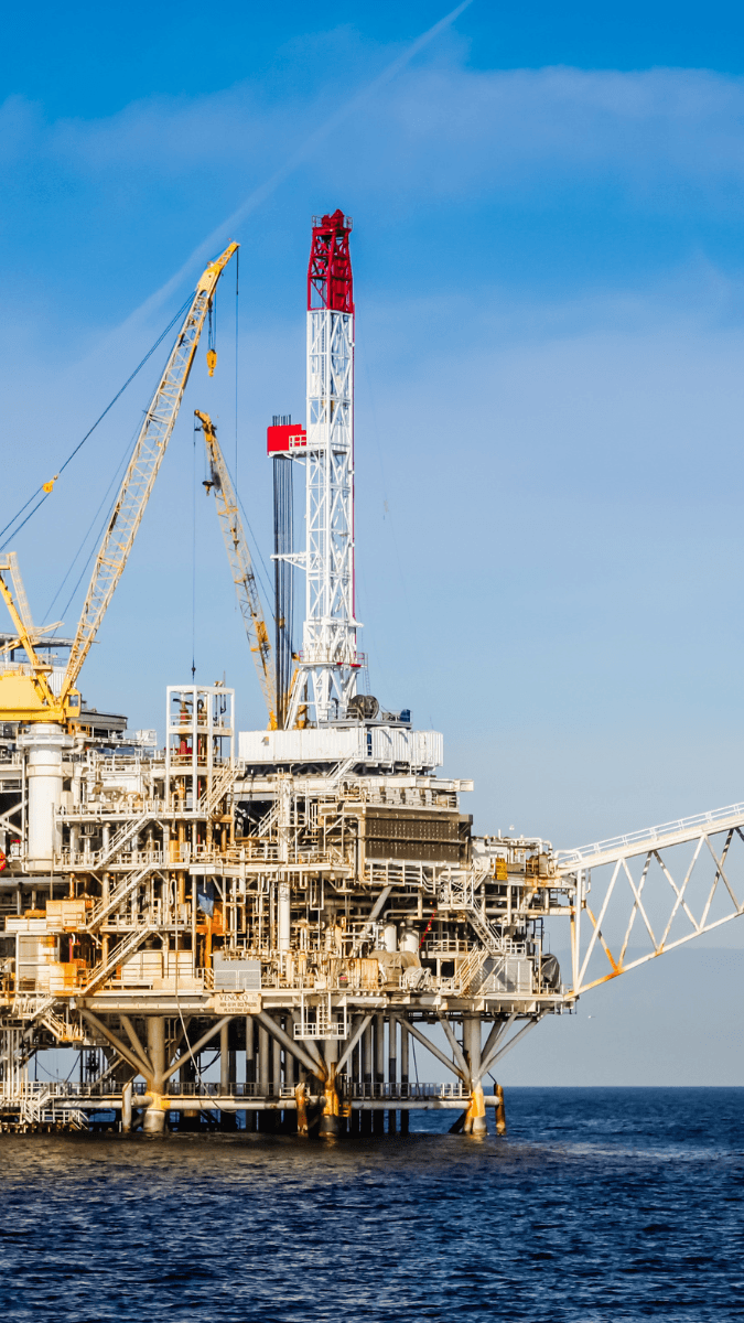 Offshore oil rig with drilling equipment and cranes, situated in the ocean under a clear blue sky, representing the offshore power industry.