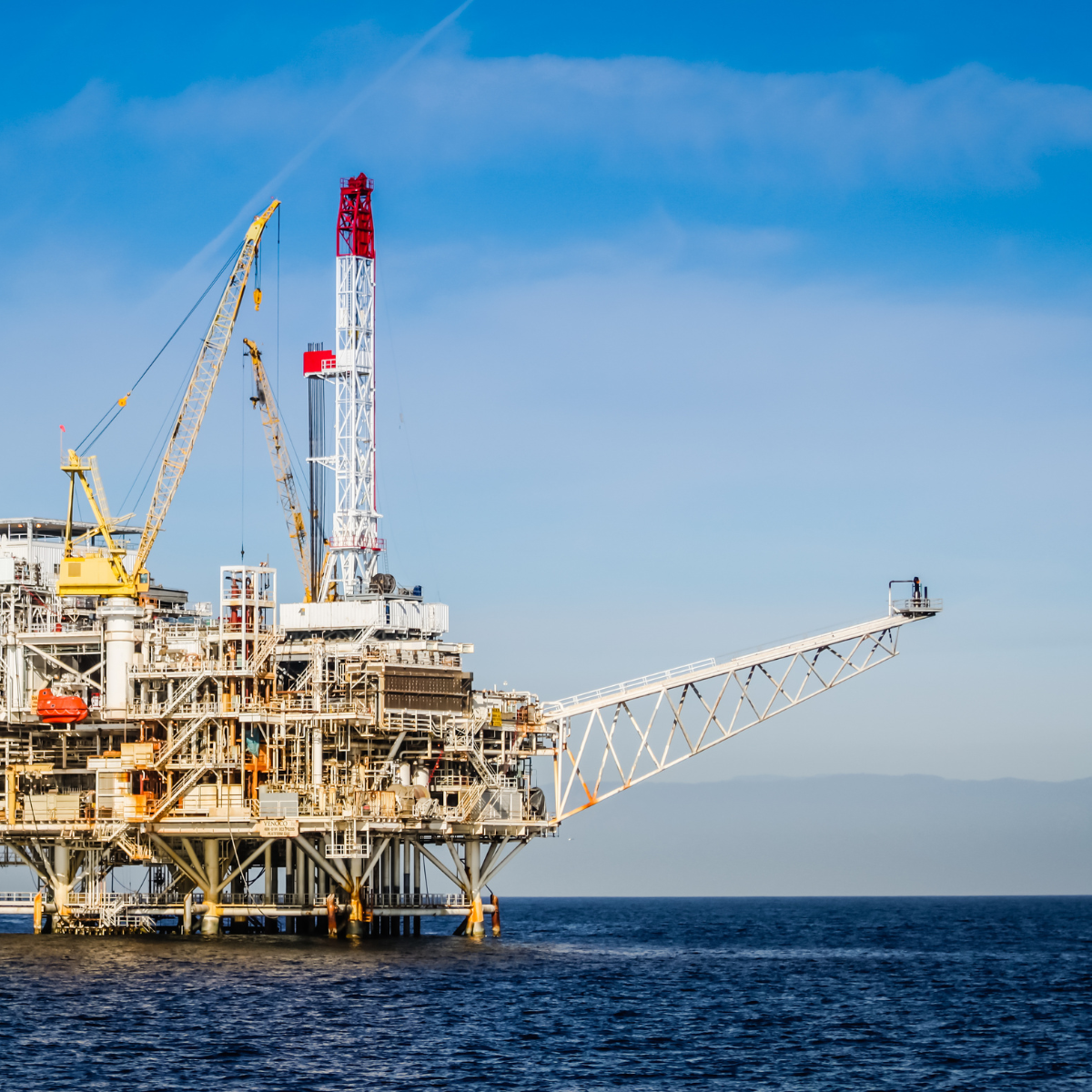 Offshore oil rig with drilling equipment and cranes, situated in the ocean under a clear blue sky, representing the offshore power industry.
