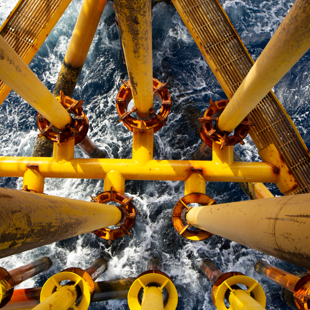 Aerial view of a yellow offshore power platform structure above turbulent ocean waters, showcasing pipes and supports crucial for energy generation.