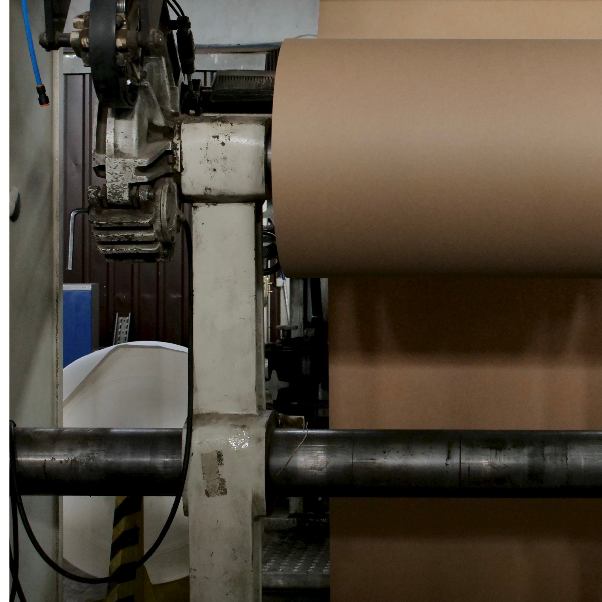 Close-up of a paper manufacturing machine displaying a large roll of brown paper being processed, illustrating the pulp and paper production process in an industrial setting.