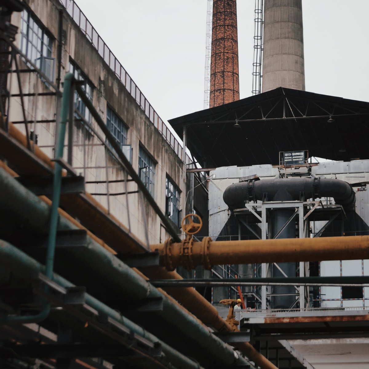 Industrial refinery structure featuring tall smokestacks, extensive piping, and a weathered exterior, illustrating the complexity of oil processing facilities.