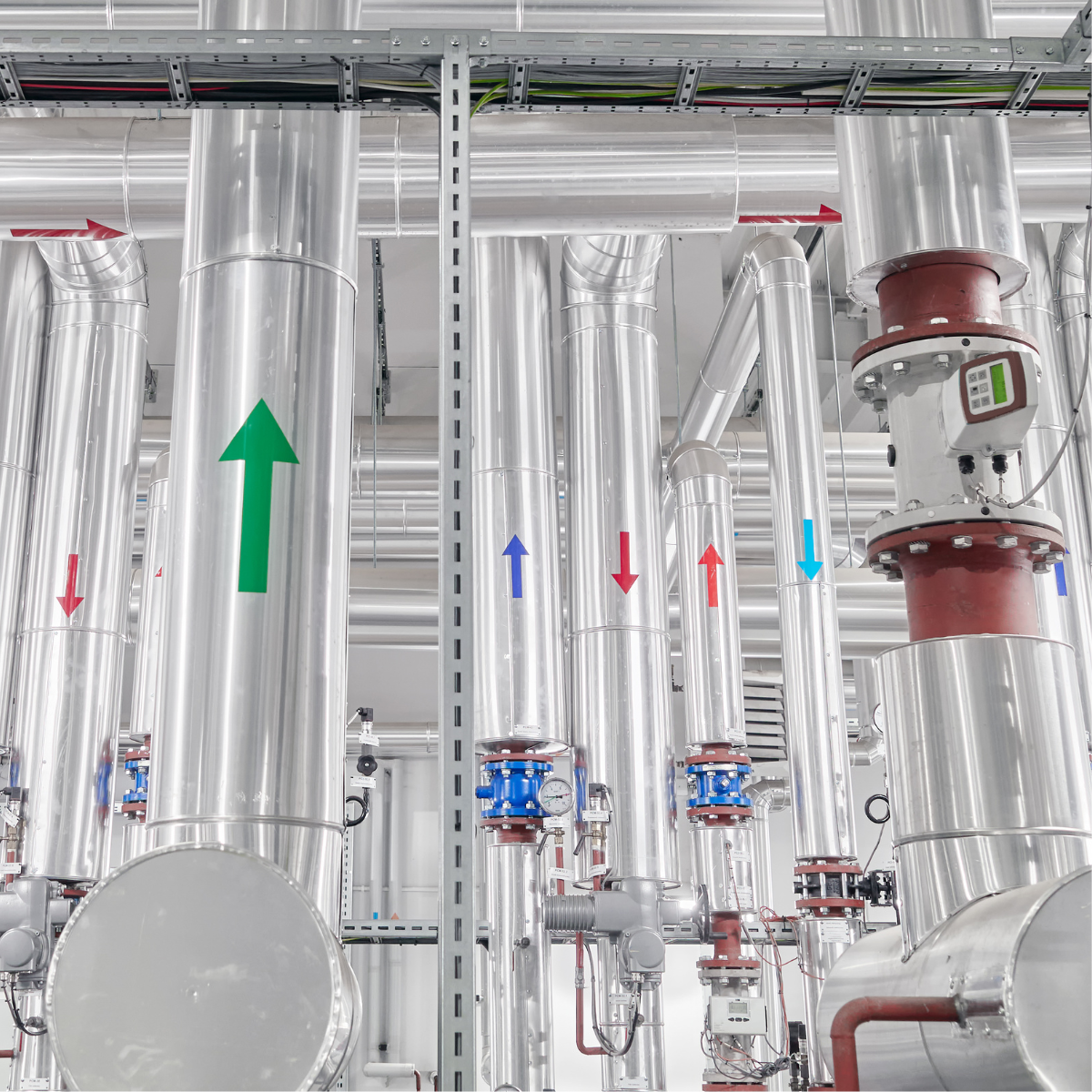 Industrial piping system in a renewable energy facility, featuring stainless steel pipes with colored directional arrows indicating flow direction, along with pressure gauges and valves for efficient energy management.
