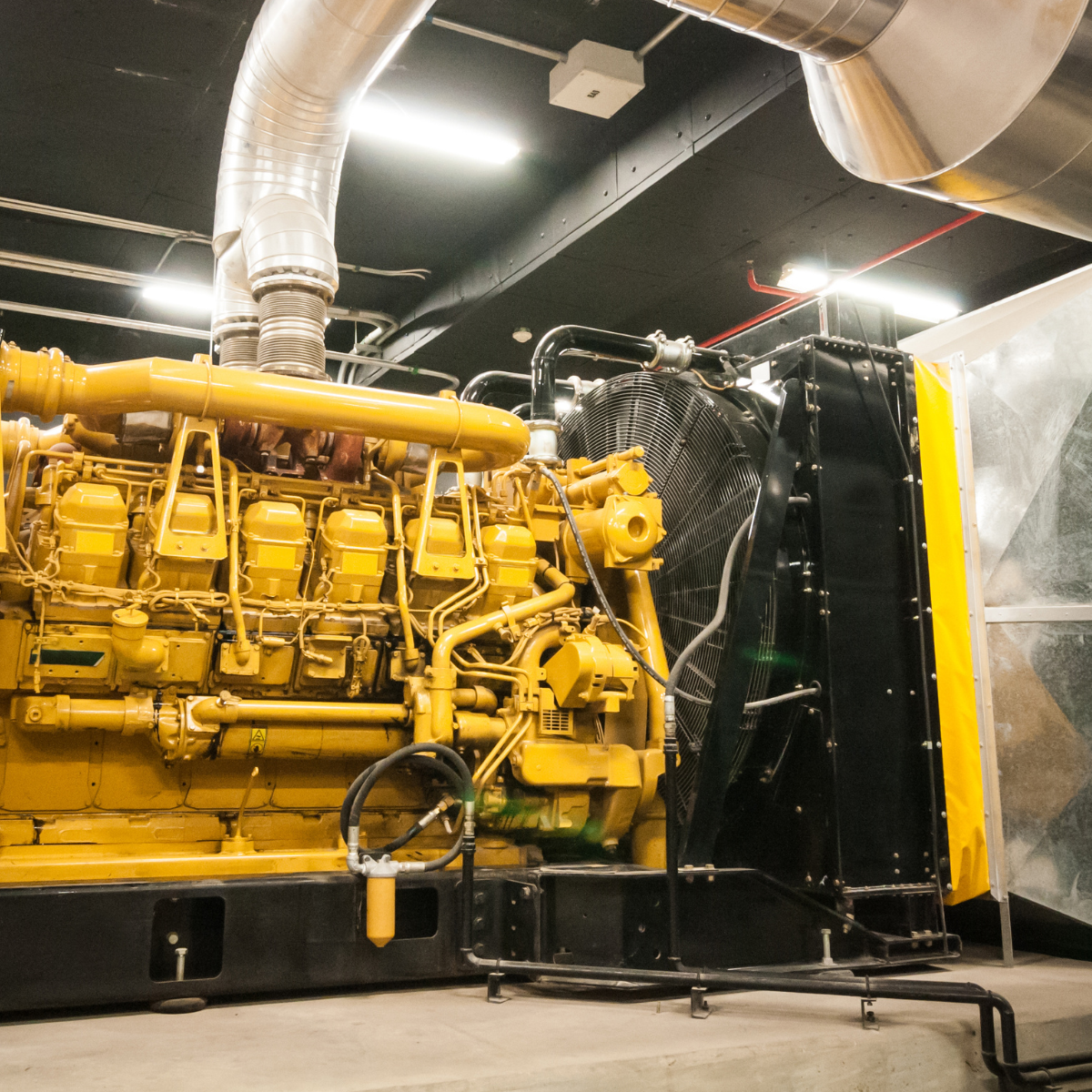 Industrial generator featuring a large yellow engine with extensive piping and cooling systems, showcased in a well-lit facility, emphasizing its robust design and functionality for power generation applications.