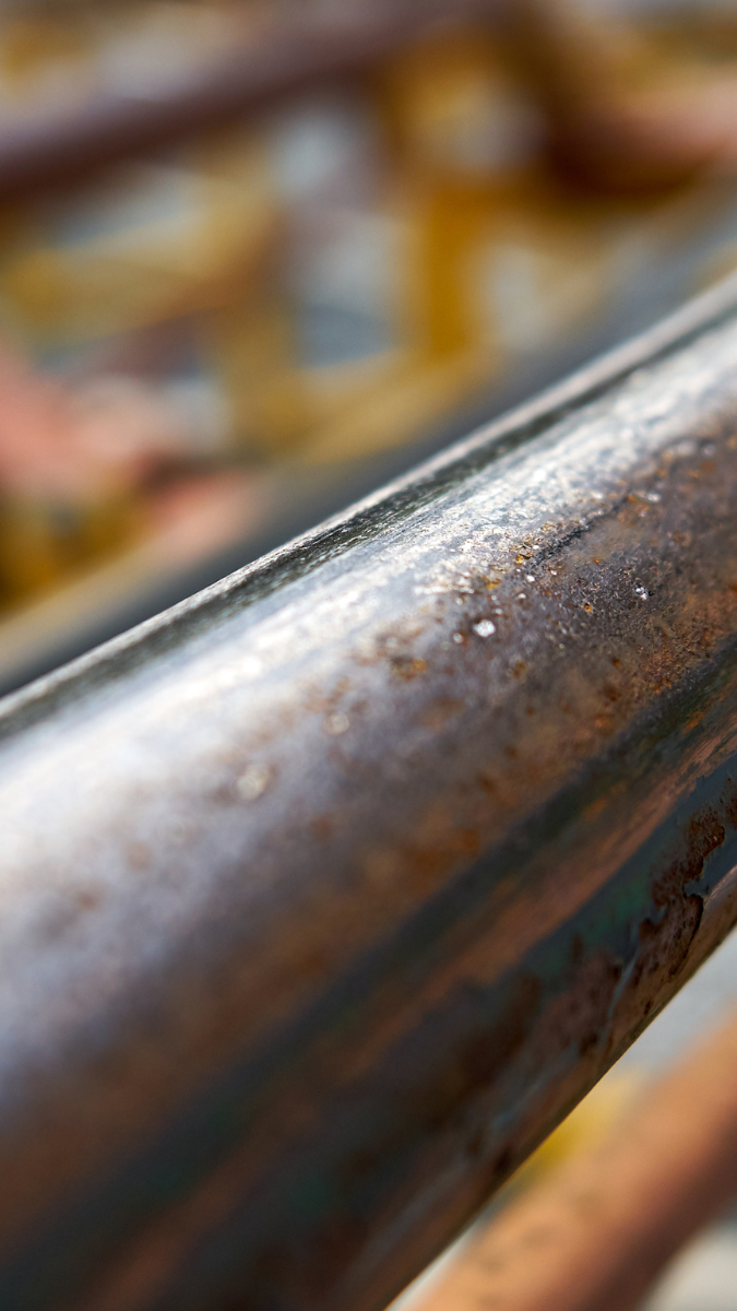 Close-up of a weathered train rail, showcasing its metallic surface with rust and wear, set against a blurred background of railway infrastructure.