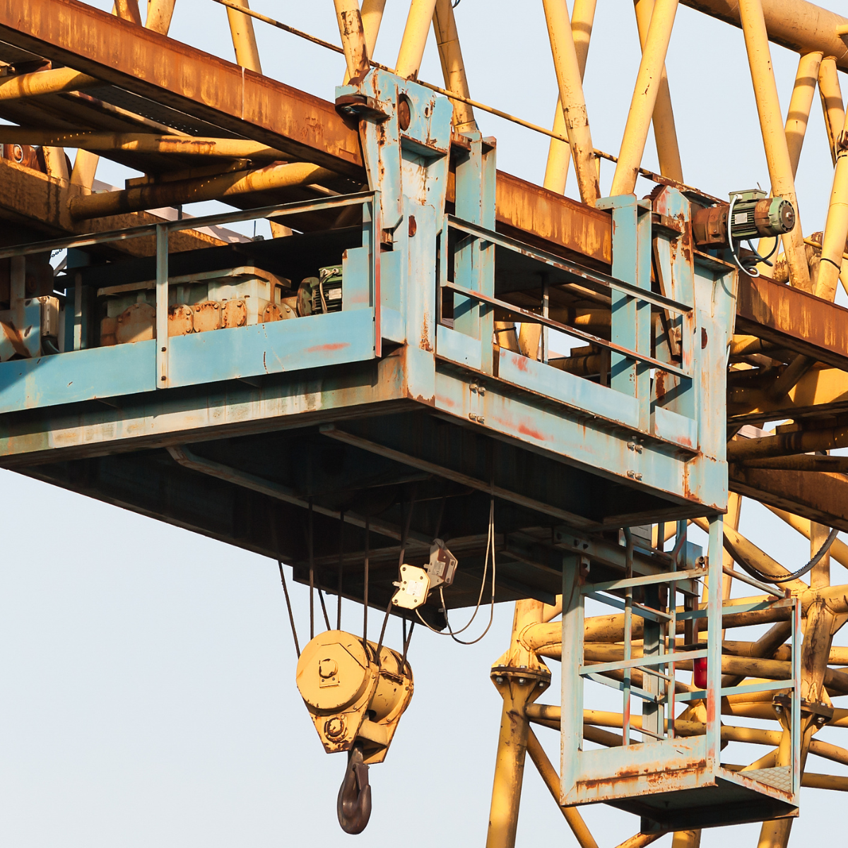 Industrial winch system mounted on a crane, featuring a blue control platform, yellow cables, and a hook for lifting heavy loads. Ideal for construction and heavy machinery operations.